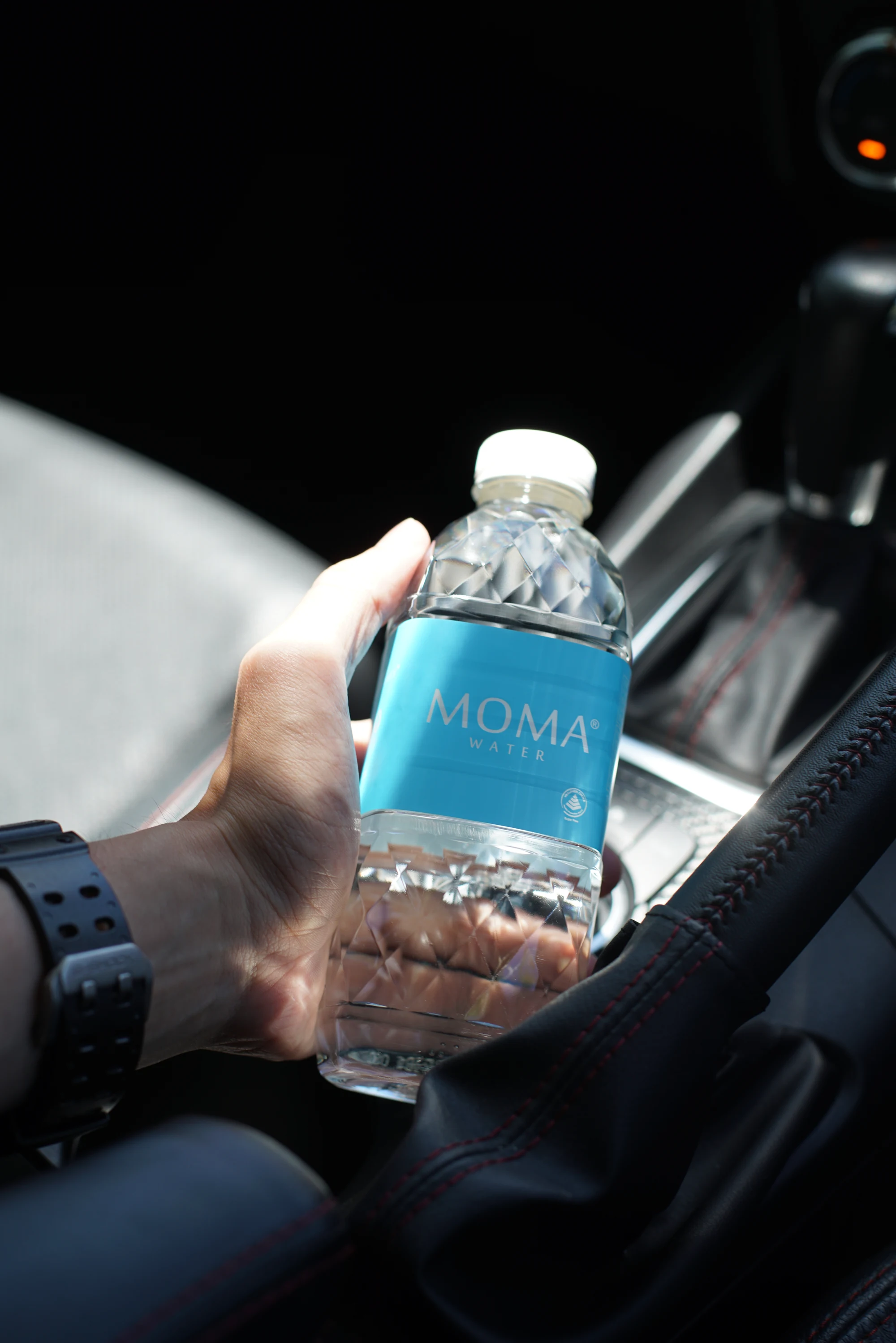 A MOMAwater bottle in hand in the car — low enough to sit beside the gear shift.