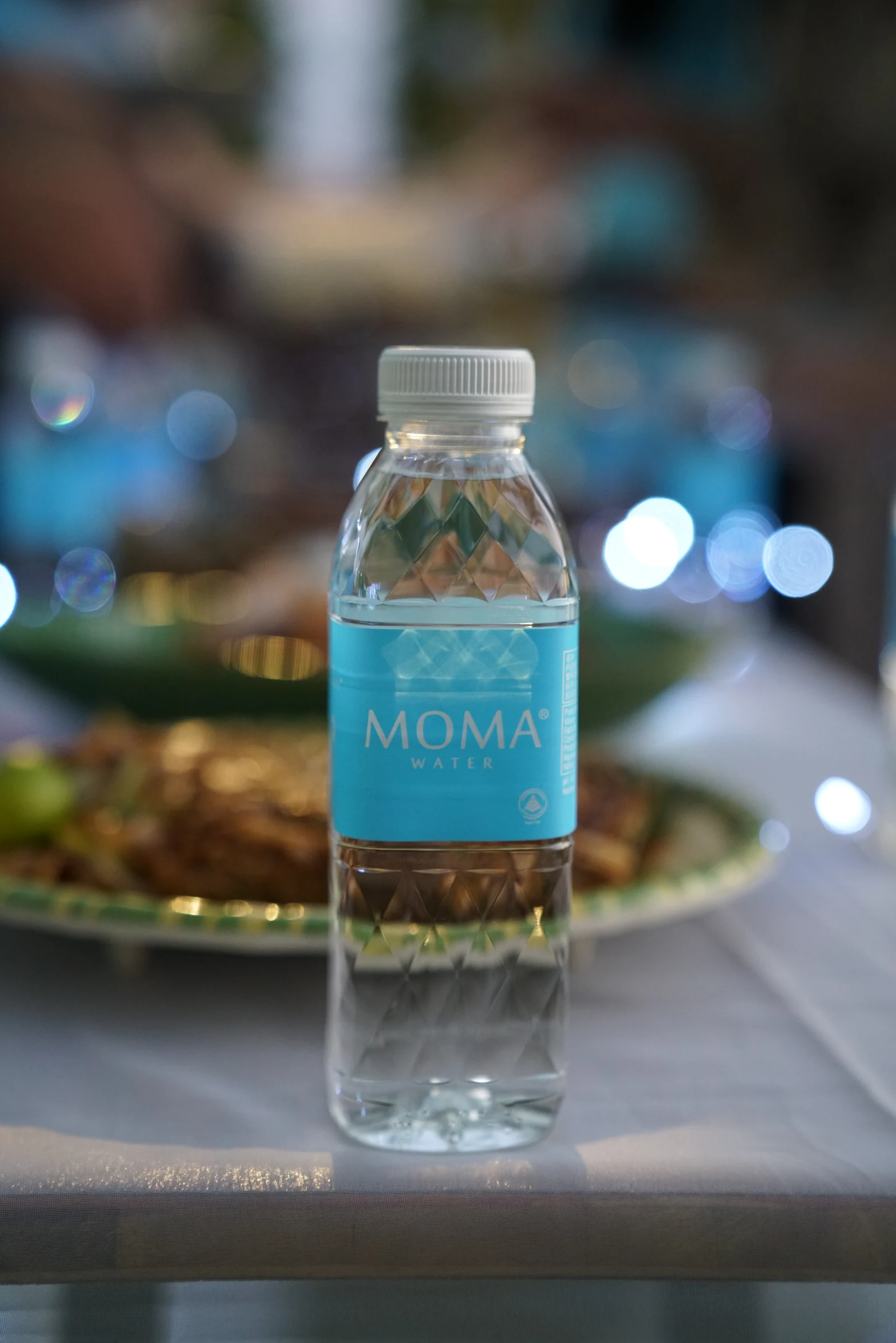 A MOMAwater bottle standing at a lakeside place setting at dusk.