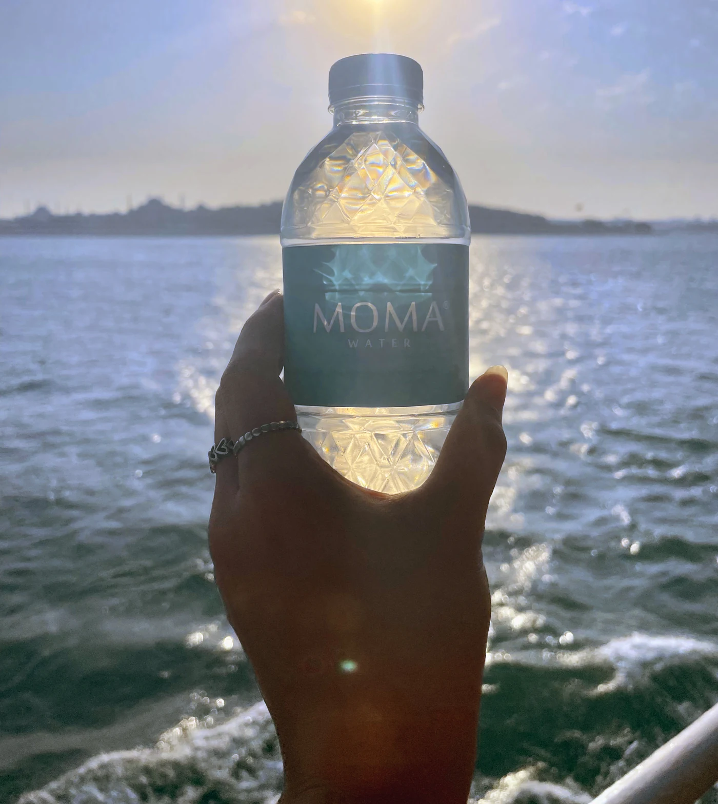 A MOMAwater bottle held against the evening sea, sunlight through the facets.